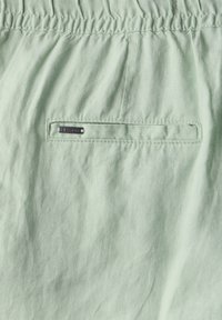 Ljusgrön tyg med en texturerad yta. Har en elastisk midja och en liten metall-logotagga sydd på en bakficka.