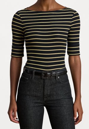 Personne portant un haut noir à manches courtes avec des rayures beiges horizontales, un jean noir taille haute et une ceinture noire avec une boucle rectangulaire.