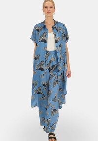 Jasnoniebieski jedwabny zestaw z wzorzystą koszulą i spodniami o szerokich nogawkach z czarnymi liściastymi wzorami. Okrągłe guziki i luźny krój.