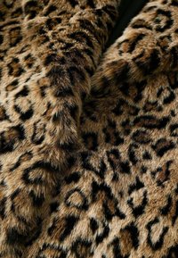 Tessuto in pelliccia sintetica con stampa leopardata, caratterizzato da una texture morbida con sfumature di marrone e nero, che presenta una combinazione di aree a motivo e a tinta unita.