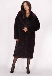 Lang, mørk burgunder faux fur frakke med bred krave og åben foran. Har en blød tekstur og knælangt design, der er parret med sorte hæle.