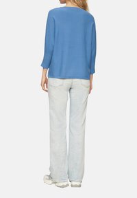 Blauer gerippter Strickpullover mit Dreiviertelärmeln, kombiniert mit hellblauen, verwaschenen Jeans und beigen Sneakers. Rückansicht des Outfits.