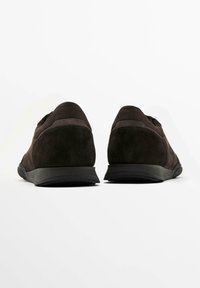 Mörkbruna sneakers i mocka med låg profil, svart gummisula och sydda detaljer. Har en strukturerad yta och vadderad krage.