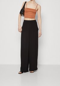 Orange patterned crop top with black wide-leg trousers. The top features a wavy design, while the trousers have side pockets and a relaxed fit.
