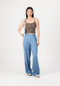 Un haut court en imprimé léopard, un pantalon large bleu clair, des ballerines beiges et un sac à épaule blanc. Textures lisses et éléments de design décontractés.