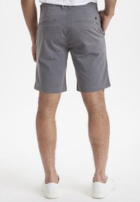 Bermudas de algodón gris con corte recto, dos bolsillos traseros y una textura suave, combinadas con zapatillas blancas.