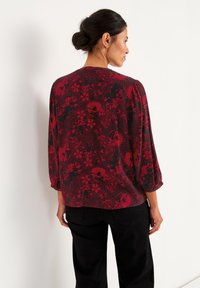 Rød og sort blomsterbluse med lange ærmer, afslappet pasform, tekstureret stof, med et varieret blomsterdesign og subtile prikkede detaljer.