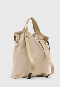 Mochila de nailon beige con dos correas de hombro duraderas, acentos de costura roja y una forma simple y estructurada con apertura con cremallera.