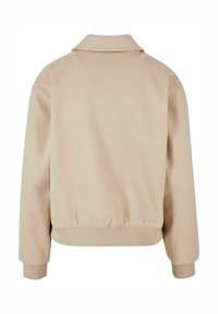 Beige fleecejakke med krage, lange ermer, elastisk liv, og myk tekstur. Enkelt og minimalistisk design.