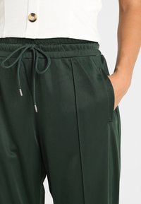 Gröna satintrosor med elastisk midja, dragsko och sidofickor. Har framvikningar och en slät textur.