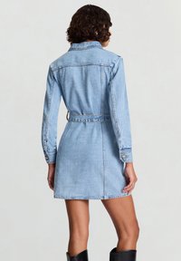 Vestito di denim azzurro chiaro con maniche lunghe, vita con cintura e polsini con bottoni. Presenta un colletto classico e una vestibilità sagomata.