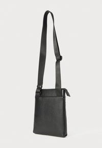 Borsa a tracolla nera in pelle con tracolla regolabile, chiusura con zip e texture liscia. Presenta un design minimalista e una forma rettangolare.
