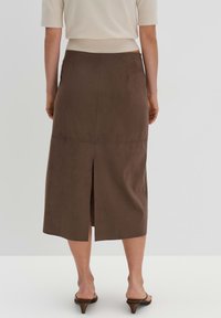 Gonna midi in suede marrone con spacco posteriore, vita piatta e design senza cuciture, abbinata a tacchi aperti.