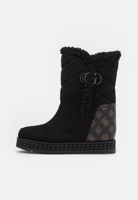 Sort ankelstøvle med quiltet design, kunstpelskrave, præget brunt mønster på siden og en sort logoaccent, med en tekstureret sål.