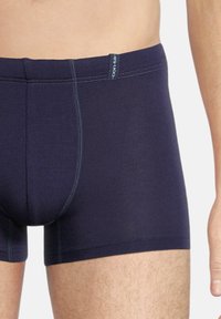 Navy boxer briefs made of stretch fabric with a snug fit, featuring contrasting stitching and a logo tab on the waistband.
