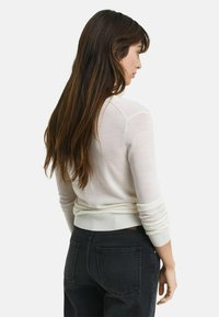 Pull léger en crème avec un col rond, des poignets côtelés et un ourlet. Associé à un jean foncé, montrant une coupe décontractée et une texture douce.