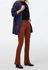 Gilet en tricot bleu avec des accents orange, associé à un pantalon évasé marron et des bottines noires. Design texturé et à ouverture frontale.