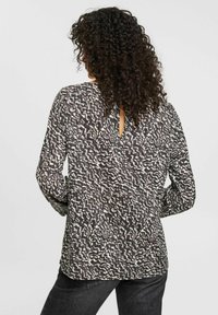 Blusa a maniche lunghe con un motivo astratto in bianco e nero, caratterizzata da un dettaglio a oblò sul retro e un tessuto morbido e testurizzato.