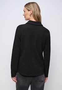 Svart texturerad långärmad skjorta med krage. Har subtila mönsterdetaljer och en avslappnad passform, med rundad nederkant bak.