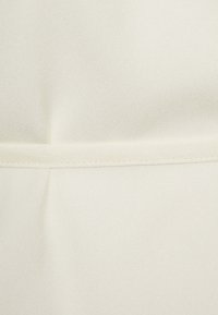 Krämfärgat tyg med en mjuk struktur, med en subtil glans och en horisontell sömdetalj över mitten.