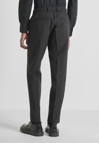 Pantalones negros a medida con cinturilla elástica, dos bolsillos traseros y un diseño estilizado. Presentan una textura suave y una silueta delgada.