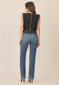 Schwarzes Spitzenoberteil mit gewellten Kanten, das einen Reißverschluss hinten hat, kombiniert mit gerade geschnittenen blauen Denim-Jeans und schwarzen High Heels.