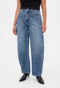 Kõrge vöökohaga, laiantie sinised teksapüksid heleda pesuga, millel on viis taskut ja nööpidega suletav eesmine osa. Sile tekstuur, klassikaline disain.