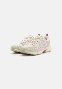 Lätta träningsskor gjorda av mesh och syntetiska material, med en beige färg och rosa detaljer, texturerad yta och framträdande snören.