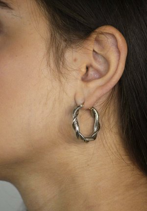 Orecchini a cerchio in tonalità argento con un design intrecciato, caratterizzati da una superficie testurizzata e un piccolo accento dorato vicino alla cerniera.