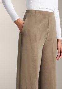 Svetlohnedé nohavice s širokými nohavicami vyrobené z ribkovanej tkaniny, s vysokým pásom a bočnými vreckami. Textúra je hladká s jemnými vertikálnymi pruhmi.