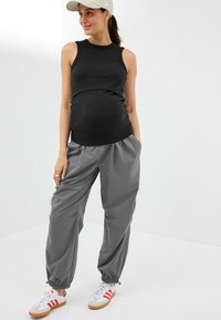 Top sans manches noir, pantalon à cordon de serrage gris clair et baskets blanches avec des rayures rouges. Tissu lisse, coupe décontractée et poignets aux chevilles.