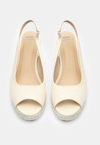 Bež odprti petni čevlji z wedge peto, izdelani iz platna, s usnjenim oblogo in pletenim jutenim podplatom; vsebujejo slingback obliko za podporo.