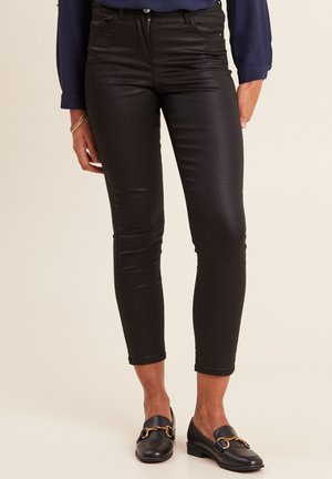 Pantalons noirs ajustés avec une finition brillante, dotés d'une fermeture éclair, d'un design à cinq poches et d'une longueur cropped, associés à des mocassins noirs.