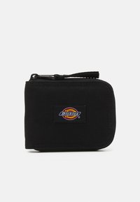 Billetera de tela negra con cierre de cremallera, que presenta un prominente parche con el logo de Dickies en la parte frontal. Forma cuadrada compacta con una superficie texturizada.