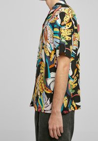 Chemise à manches courtes en tissu léger avec un imprimé tropical multicolore vif sur fond noir.