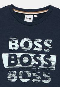T-shirt bleu marine en coton, avec un texte superposé "BOSS" en blanc avec un effet vieilli. Encolure ronde et manches courtes.