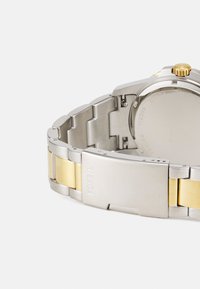Montre en acier inoxydable avec un bracelet bi-couleur présentant des maillons argentés et dorés. Le fermoir est gravé du nom de la marque "FOSSIL."