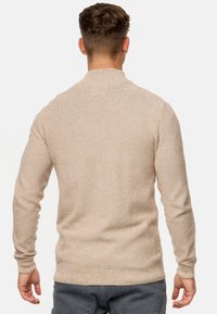 Beiger Strickpullover mit strukturierter Optik, langen Ärmeln und rundem Ausschnitt, schmal geschnitten und mit gerippten Bündchen.