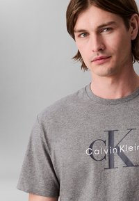 Γκρι βαμβακερό T-shirt με κοντά μανίκια, με σκούρο μπλε λογότυπο "CK" και την επιγραφή "Calvin Klein" στο μπροστινό μέρος. Μαλακή υφή.