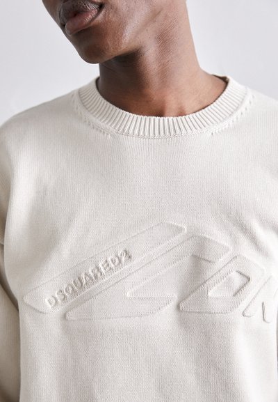Sweatshirt en tricot beige clair avec un logo texturé en relief sur le devant, un col rond côtelé et des détails de couture soignés.