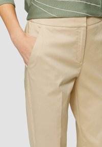 Beige broeken met een gladde textuur, voorzien van zijzakken en een getailleerde pasvorm. Gepaard met een groene bovenkant met witte strepen.