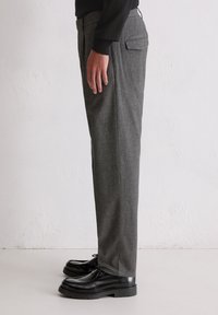 Grau maßgeschneiderte Hose aus einem strukturierten Stoff, mit geradem Bein-Design, seitlichen Taschen und Gesäßtasche, kombiniert mit schwarzen Schnürschuhen.