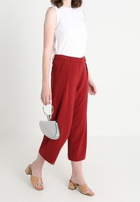 Červené kalhoty na míru s volným střihem, bílé bezrukávové tričko s očkovým detailem a malá šedá kabelka. Neutrální boty na blockovém podpatku.