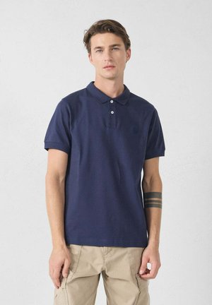 Camisa polo azul marino de algodón, con cuello, dos botones y un pequeño logo en el pecho. Manga corta y corte clásico.