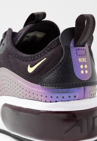 Nike sneaker featuring a black mesh upper, gold swoosh, purple gradient accents, and a visible air cushioning unit. Textured and sleek design.