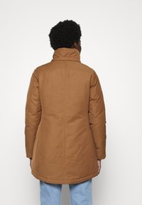 Giacca imbottita marrone con collo alto, caratterizzata da dettagli di cucitura e una texture liscia. La giacca ha una vestibilità sagomata e un orlo dritto.