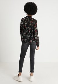 Black, floral-print sheer blouse with a ruffled neckline, long sleeves, and a slightly loose fit, paired with dark skinny jeans and white sneakers.