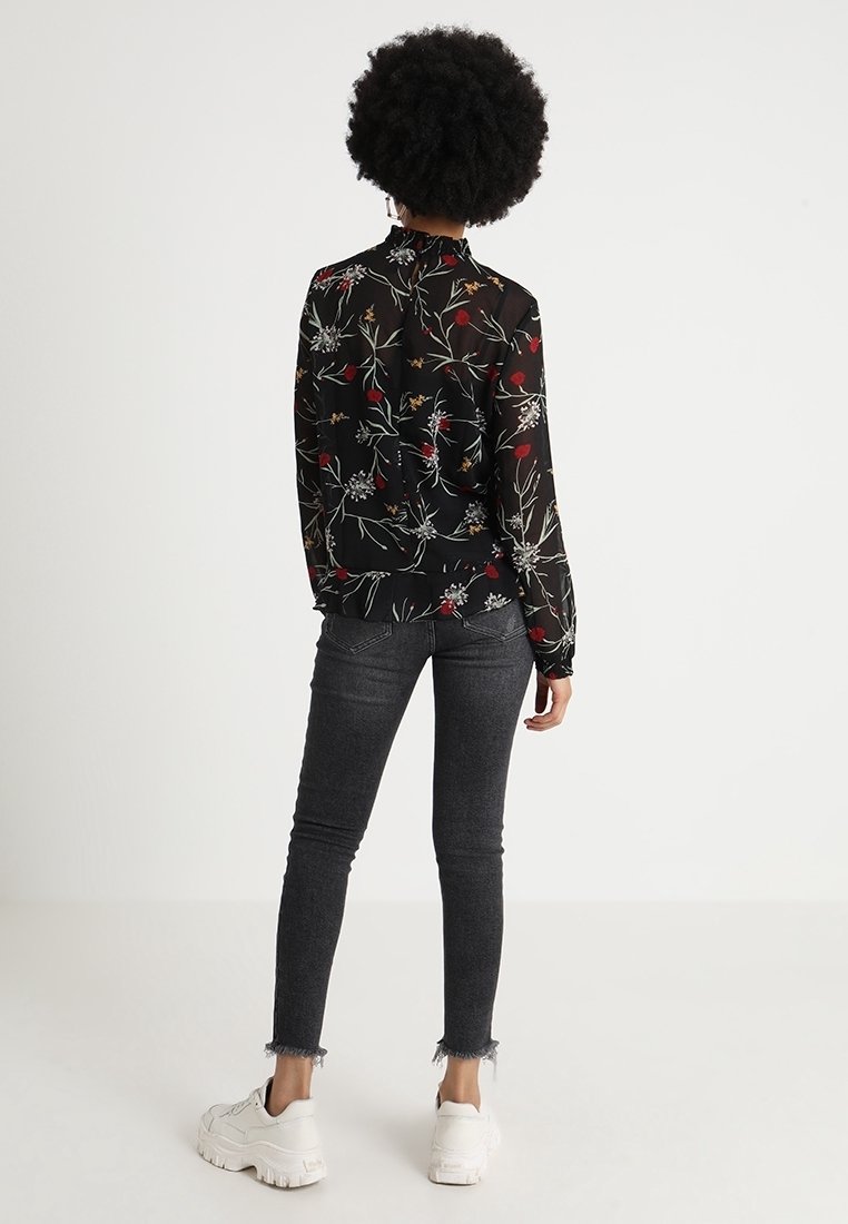 Black, floral-print sheer blouse with a ruffled neckline, long sleeves, and a slightly loose fit, paired with dark skinny jeans and white sneakers.