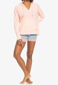 Hoodie leggero rosa con scollo a v e tasca frontale, abbinato a pantaloni corti a righe multicolori, che mostrano un fit casual e rilassato.