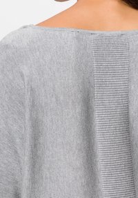 Grå stickad topp med en slät textur, bred rund halsringning och vertikala ribbade detaljer längs ryggen, vilket framhäver en avslappnad passform.